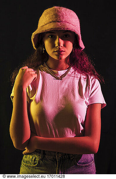 Close-up portrait of teenage girl wearing hat posing against black background