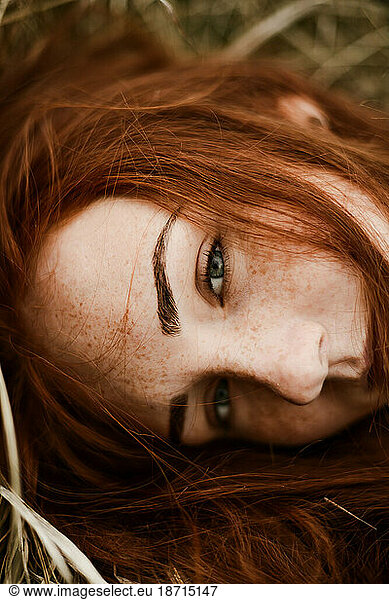 Close-up portrait of teenage girl with red head lying on grassy
