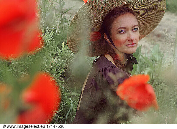 Close up portrait of woman with hat sitting among poppies flower