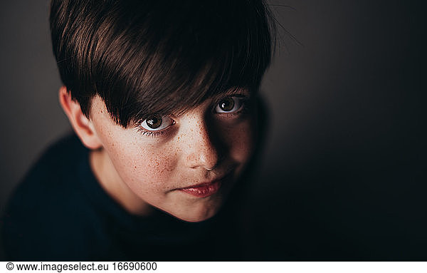 Close up portrait of young brunette boy with freckles in dark room.