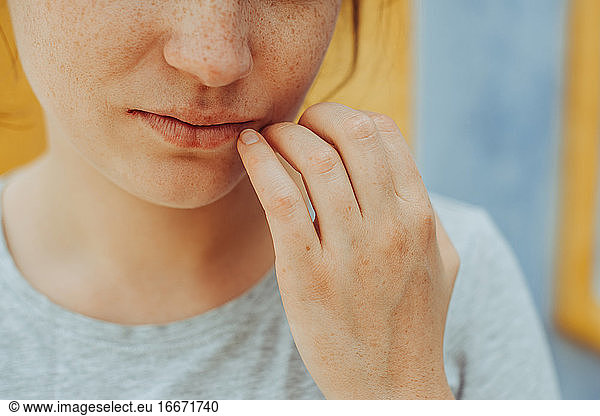 Close up portrait of young woman with freckles holding hand at lips