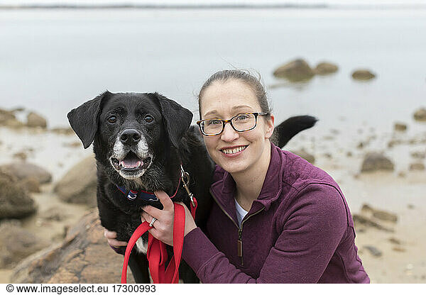 Close-up portrait smiling woman with old black lab at Cape Cod beach