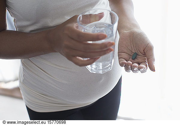 Close up pregnant woman taking vitamin with water