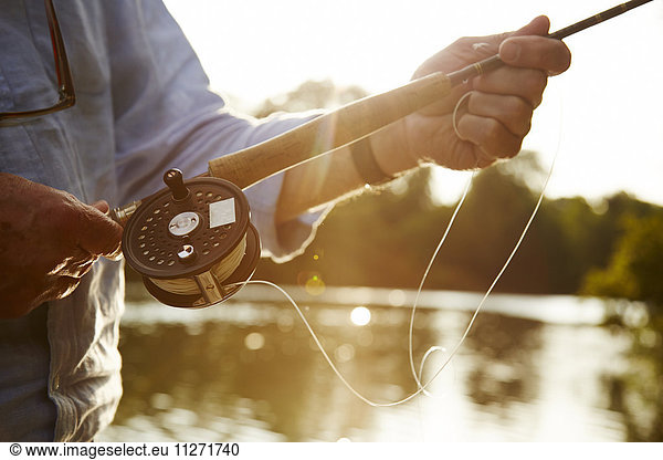 Close up senior man fly fishing at sunny river