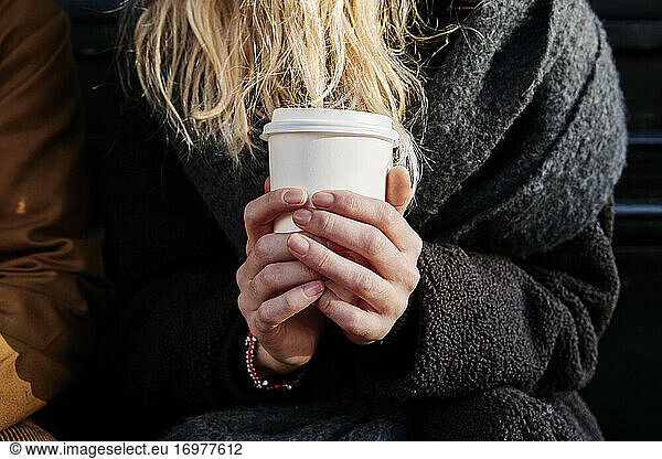close up shot of blonde female holding a paper cup of coffee with both hands