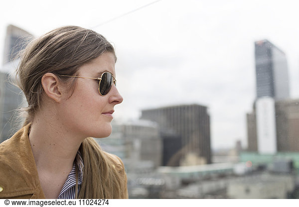 Close-up side view of businesswoman wearing sunglasses standing against buildings