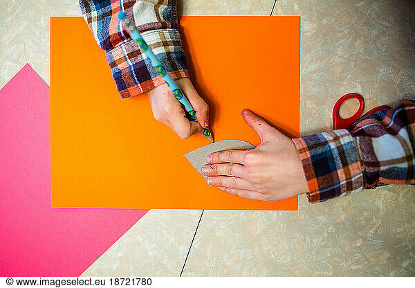 Close-up view of a child's hands tracing leaf on bright colored paper