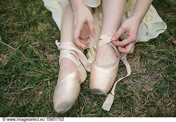 close-up view of dancer tying ribbons of toe shoes on grassy lawn