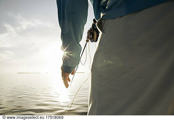 Close up view of man holding fly rod with sunburst in Florida Keys