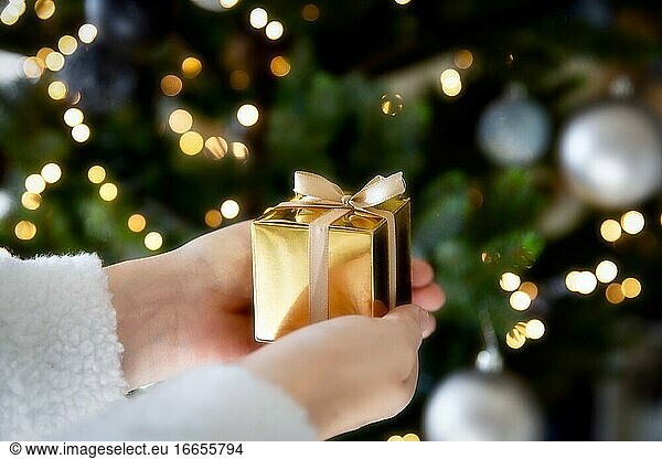Close up von Hand hält ein goldenes Geschenk-Box mit Weihnachtsbaum und Lichter auf dem Hintergrund  Gegenwart und Weihnachtsferien Konzept funkelnden Hintergrund.