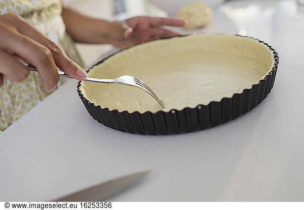 Close up woman baking poking holes into pie crust with fork