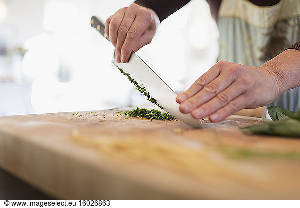 Close up woman cutting fresh herbs with knife on cutting board