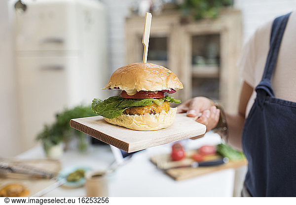 Close up woman holding cheeseburger on cutting board