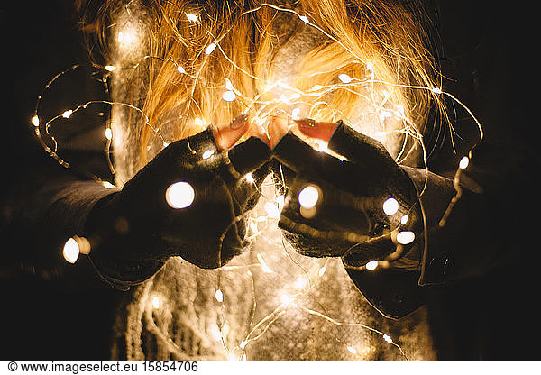 Close up woman holding Christmas lights outdoors in the dark