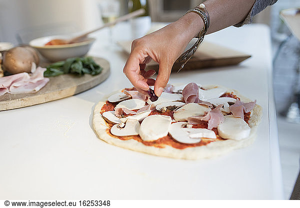 Close up woman preparing homemade pizza at kitchen counter