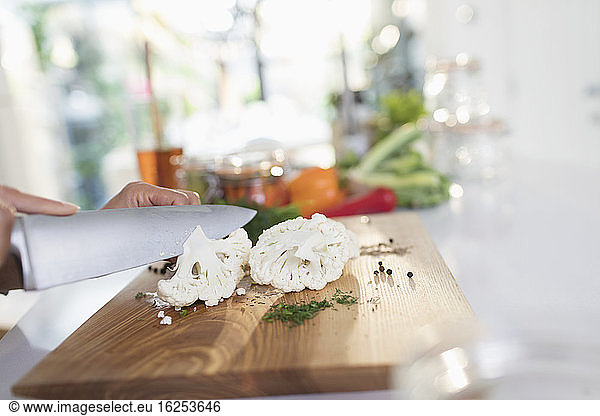 Close up woman slicing fresh cauliflower with knife on cutting board