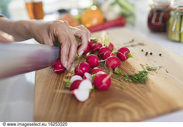Close up woman slicing fresh radishes on cutting board