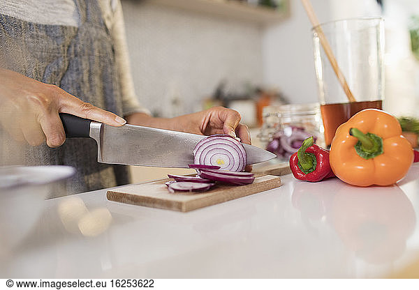 Close up woman slicing red onions on cutting board in kitchen