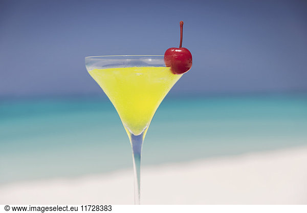 Close up yellow cocktail with cherry in martini glass on sunny tropical beach