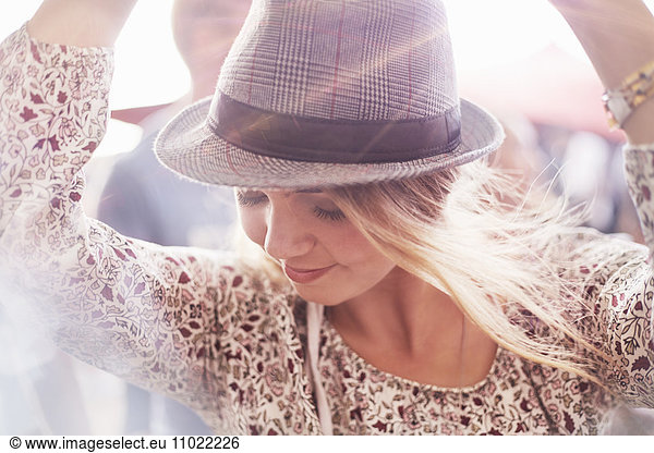 Close up young blonde woman with fedora dancing at music festival