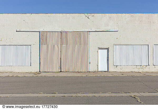 Closed warehouse building with metalwork shutters on doors and windows  and weeds growing through tarmac.