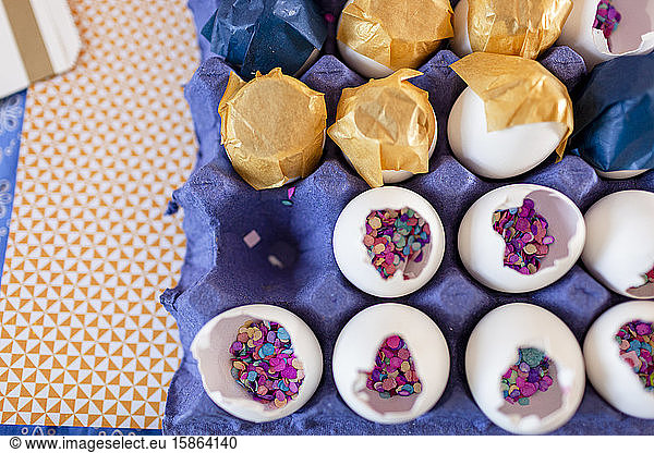 Closeup inside eggshells multicolor confettis and gold and white paper