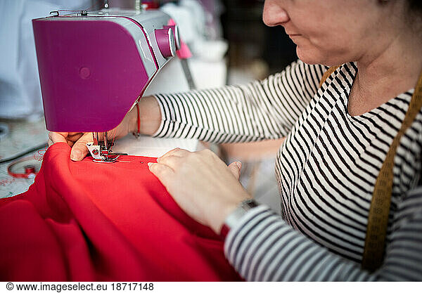 Closeup of adult woman seamstress sews clothes and put thread in needl
