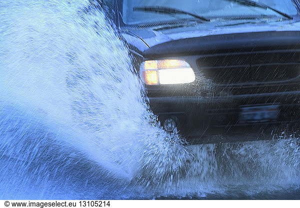 Closeup of the front end of a car going through a mud puddle.