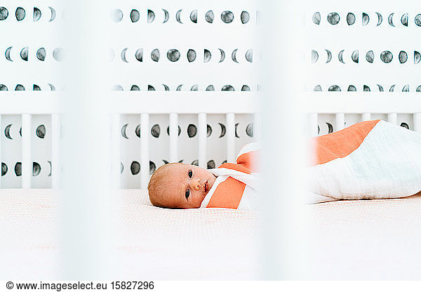Closeup portrait of a newborn baby girl laying in a modern crib