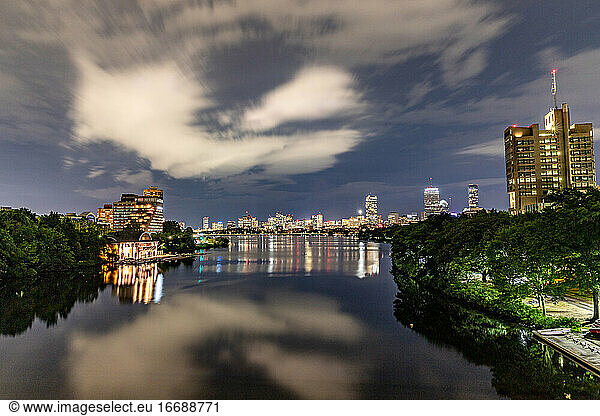 Clouds and city buildings reflecting in the river below at night.