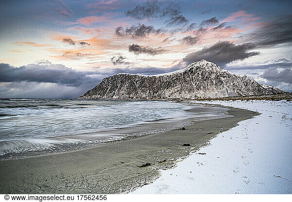 Clouds at sunset over mountain peak covered with snow and icy Skagsanden beach  Flakstad  Lofoten Islands  Norway  Scandinavia  Europe