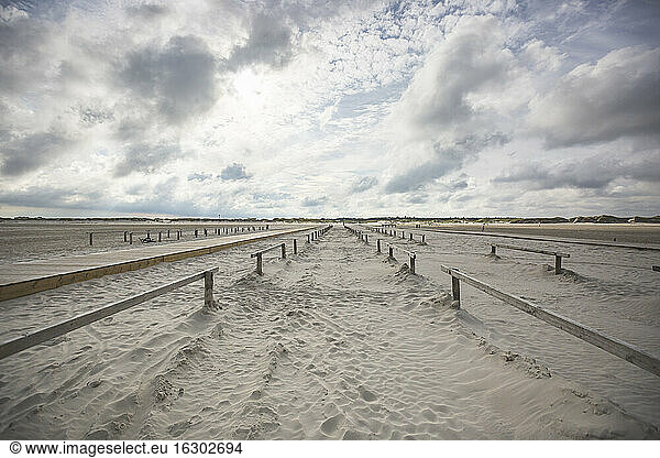 Clouds over wooden railings stretching along vast sandy beach