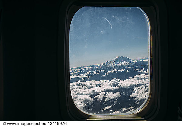 Cloudy sky amidst snowcapped mountain seen through airplane window