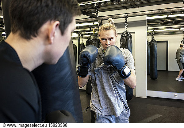 Coach and female boxer practising at sandbag in gym