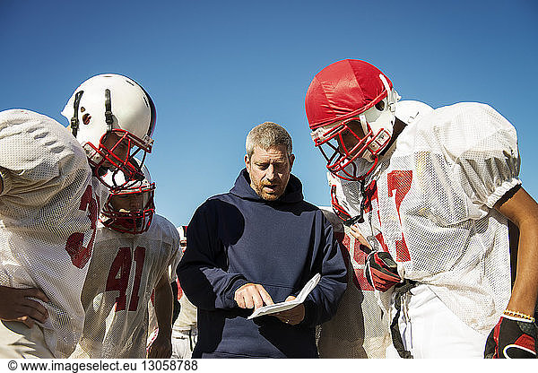 Coach sharing strategy to American football players standing on field