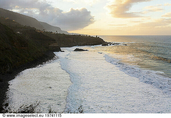 Coastline with ocean waves and cloudy sky at sunset