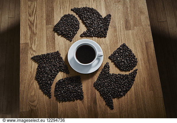 Coffee beans forming recycle symbol around coffee cup