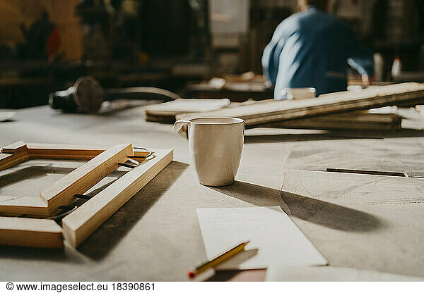 Coffee cup by wooden frame on workbench at repair shop