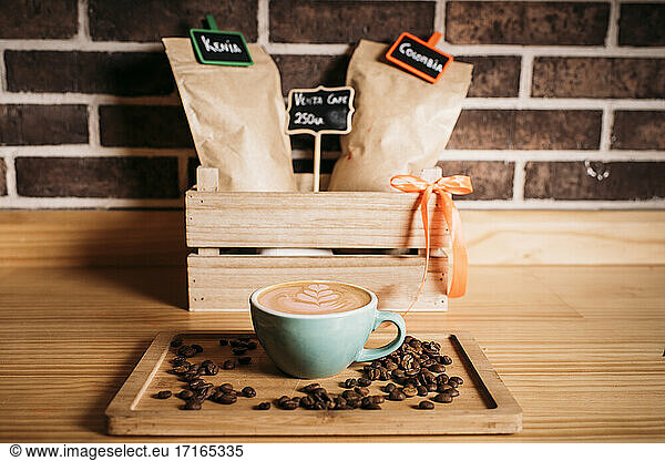 Coffee with latte art amidst coffee beans on wooden tray