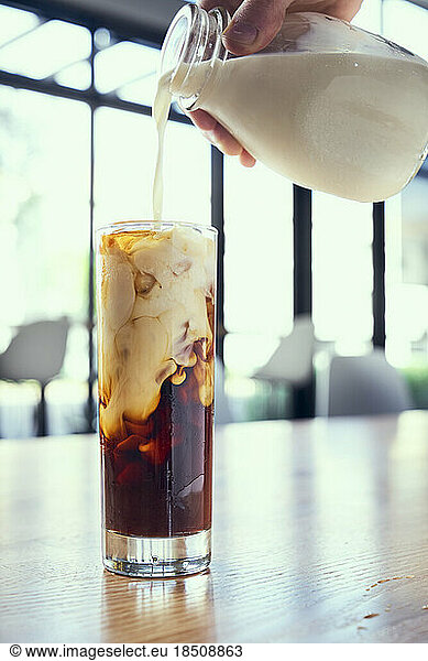 Cold brew being topped off with heavy cream on a wooden table.