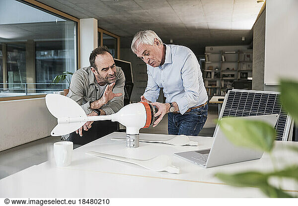 Colleague explaining engineer over wind turbine rotor at office