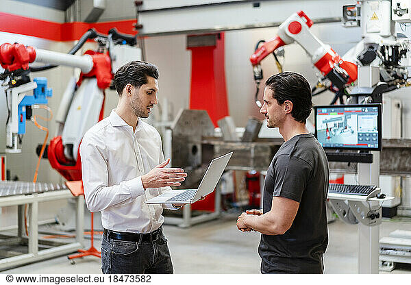 Colleague explaining technician through laptop in robot factory