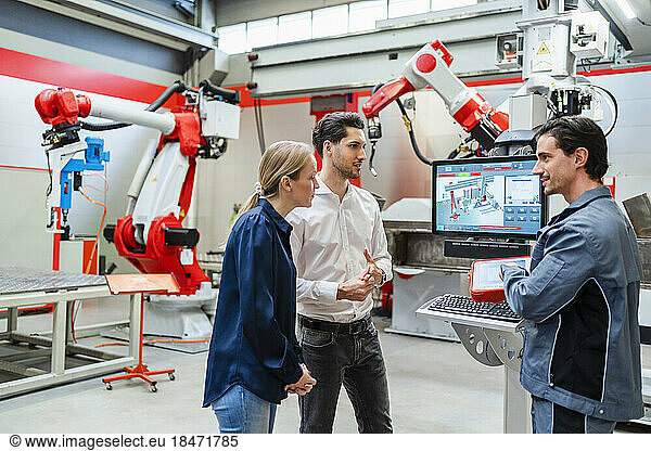 Colleagues discussing together standing at robot factory