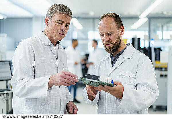 Colleagues in electronics factory discussing over motherboard