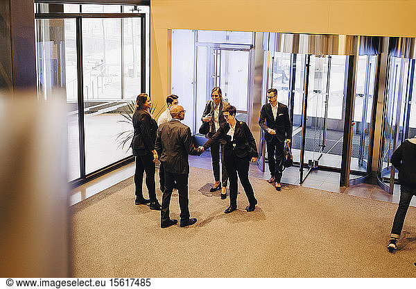 Colleagues looking at business professionals shaking hands in office lobby