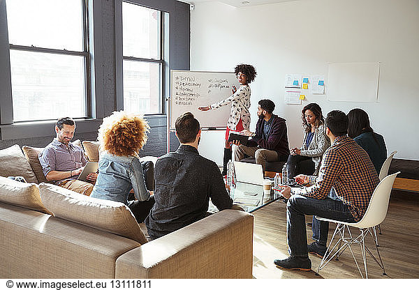 Colleagues looking at businesswoman writing on whiteboard in meeting room