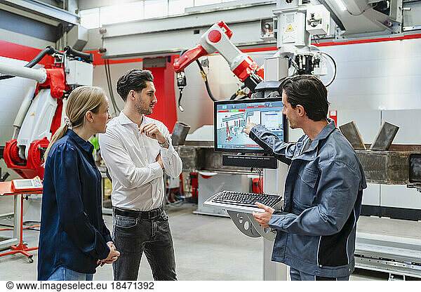 Colleagues looking at screen standing with engineer in robot factory