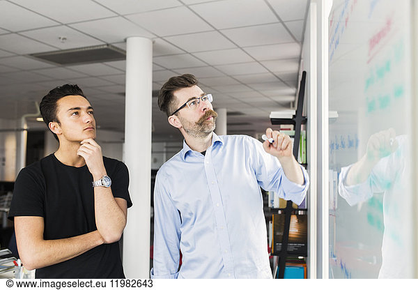 Colleagues standing next to whiteboard in office