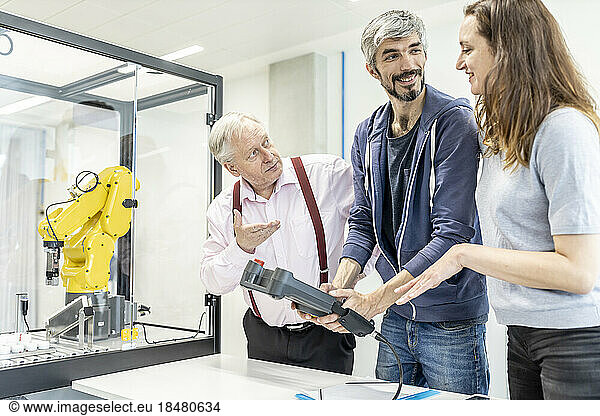 Colleagues watching woman programming robot arm with digital control