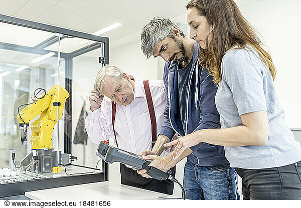 Colleagues watching woman programming robot arm with digital control
